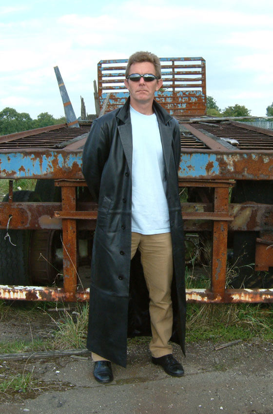 A man in a trench coat standing in front of rubble
