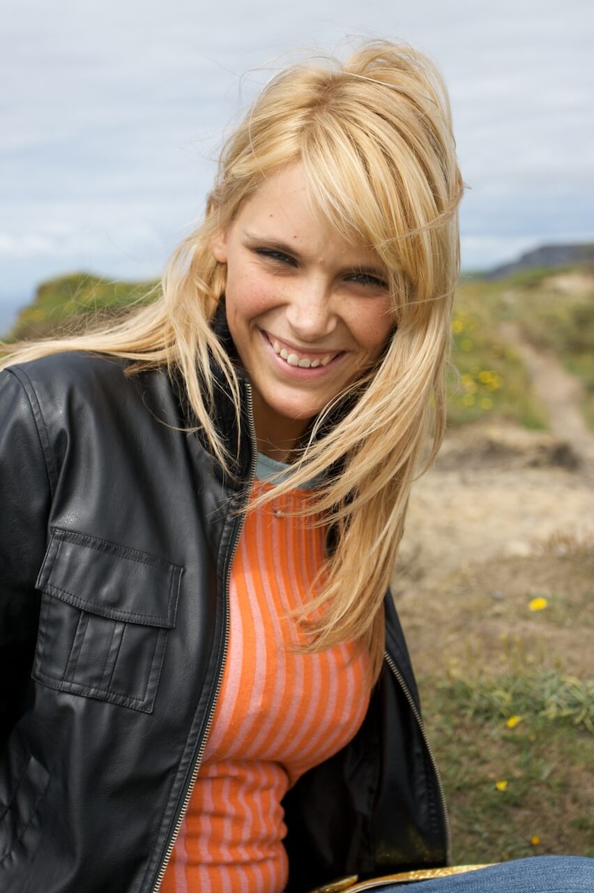A blonde woman in a black jacket and orange top