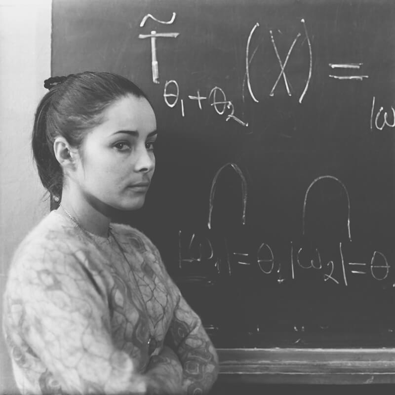 Mathematician Maria Sagaidac stands in front of a chalkboard with equations written on it