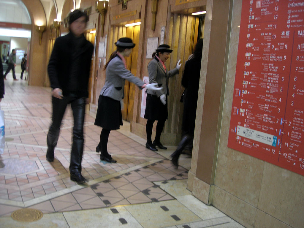 Two elevator operators in a store in Japan usher guests into the elevator