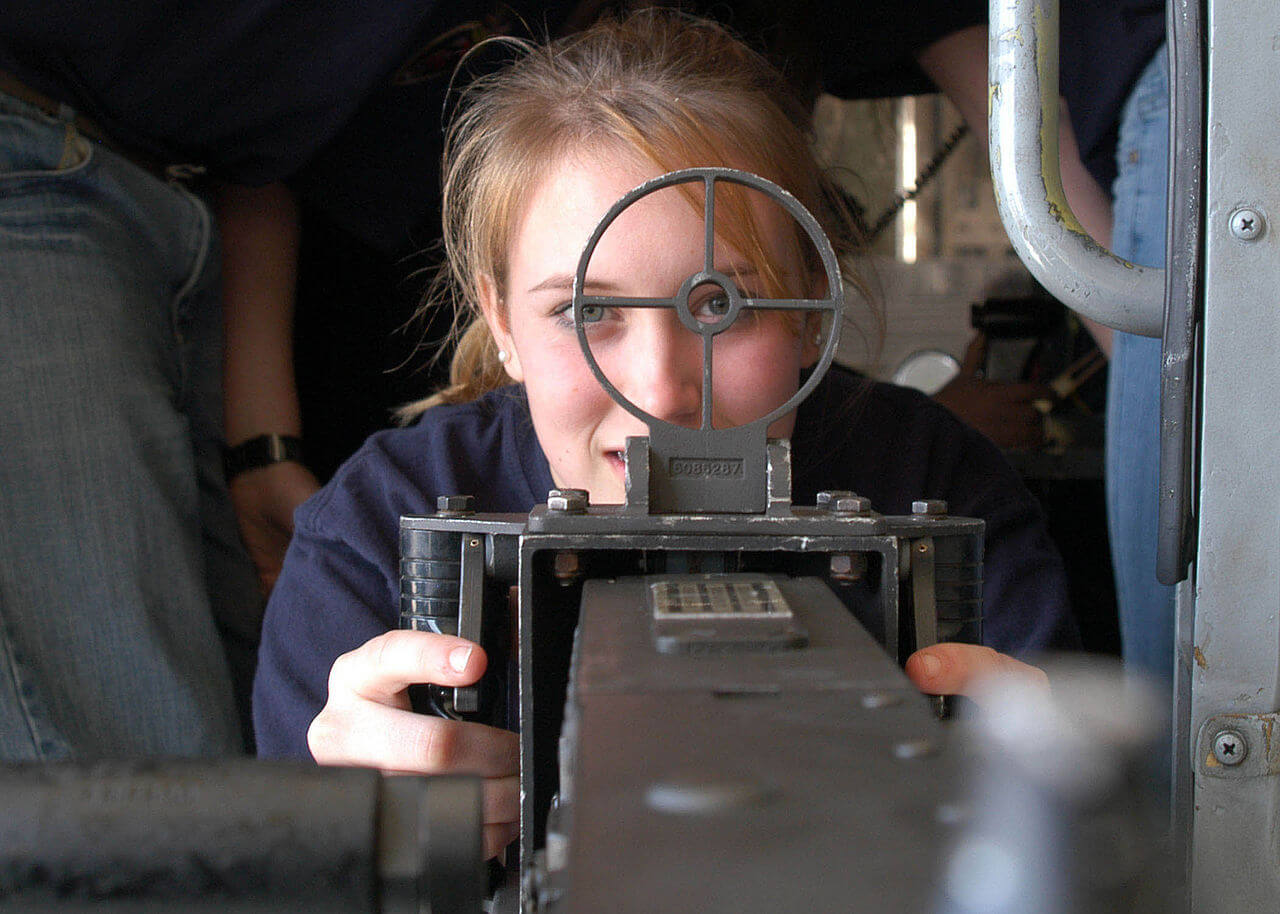 A naval cadet looks down the sight of her training weapon.