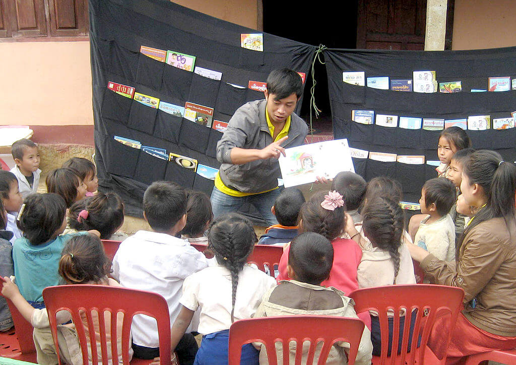 A presenter reads a book aloud to a group of children in Laos