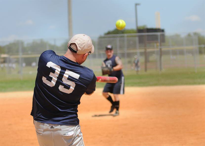 A softball player swings at an incoming pitch.