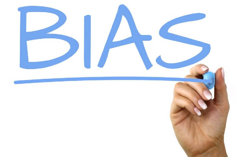 A hand writing the word "BIAS" in blue marker on a window