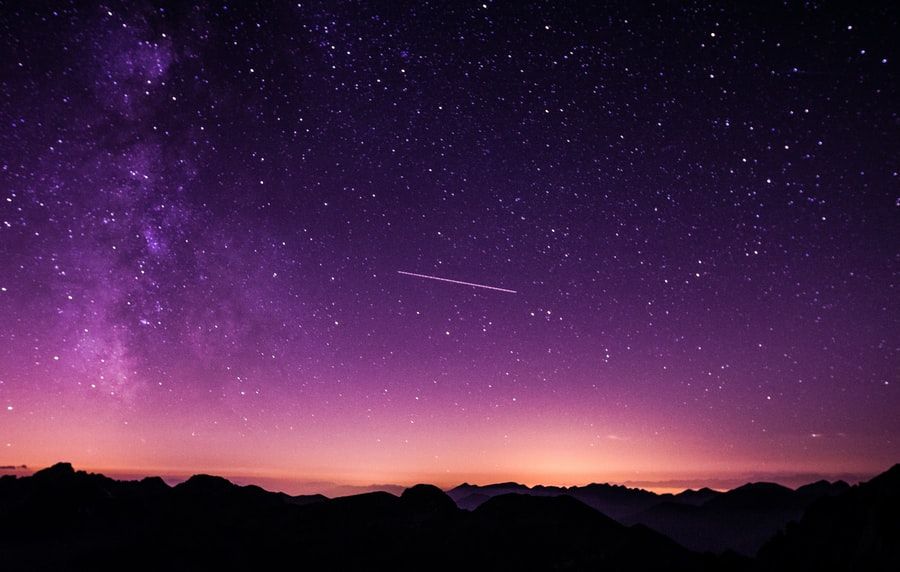 A shooting star streaks through the purple twilight sky, with mountains visible in the foreground.