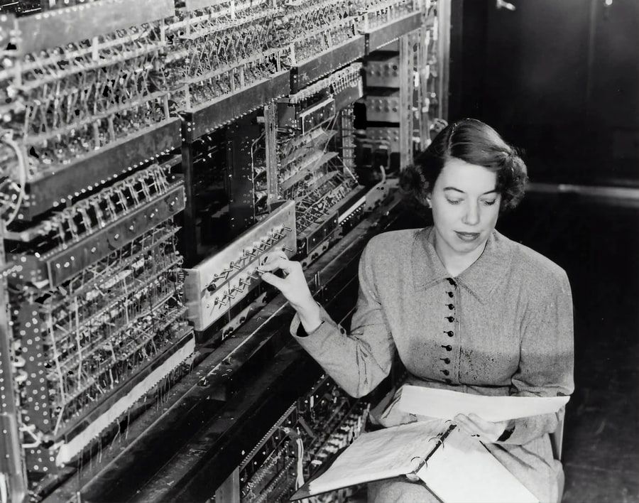 A 1950's style phone switchboard and the person who is operating it. Photo is in black-and-white.