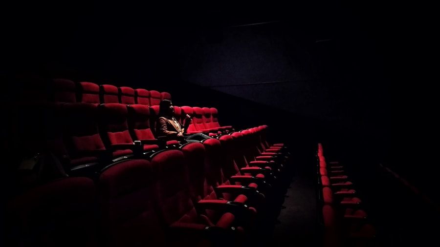 A woman sits alone in a darkened movie theatre.