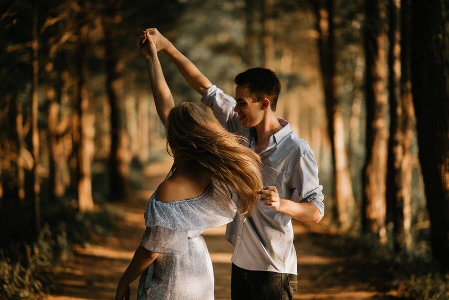 A young man and a young woman dance on a forest path at sunset.