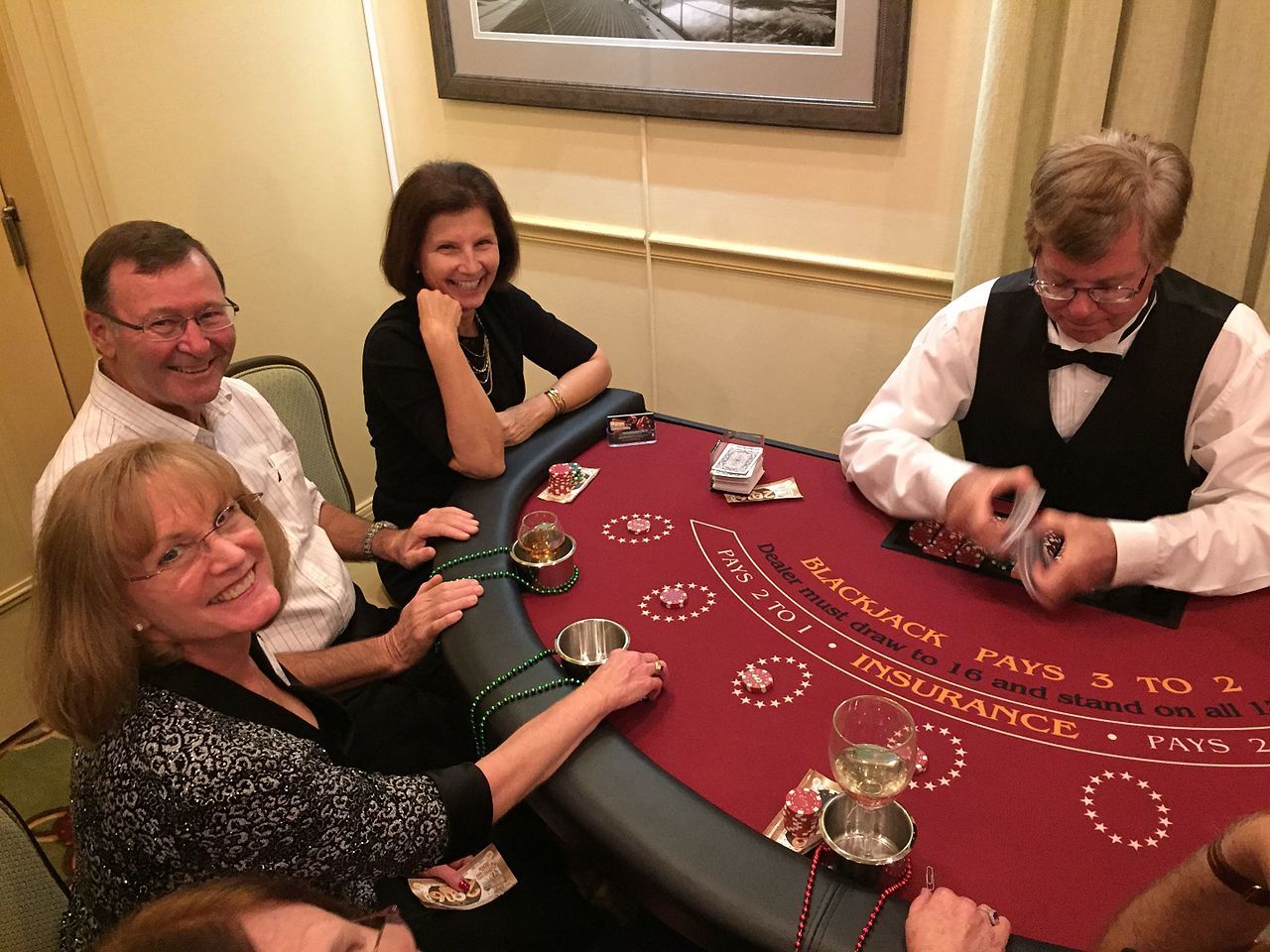 A blackjack dealer shuffles at a blackjack table as three players smile for the camera.