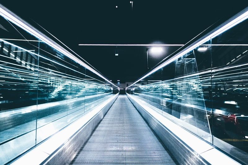 A stylized picture of a moving sidewalk, with lights elongated and shiny glass panels to the left and right.